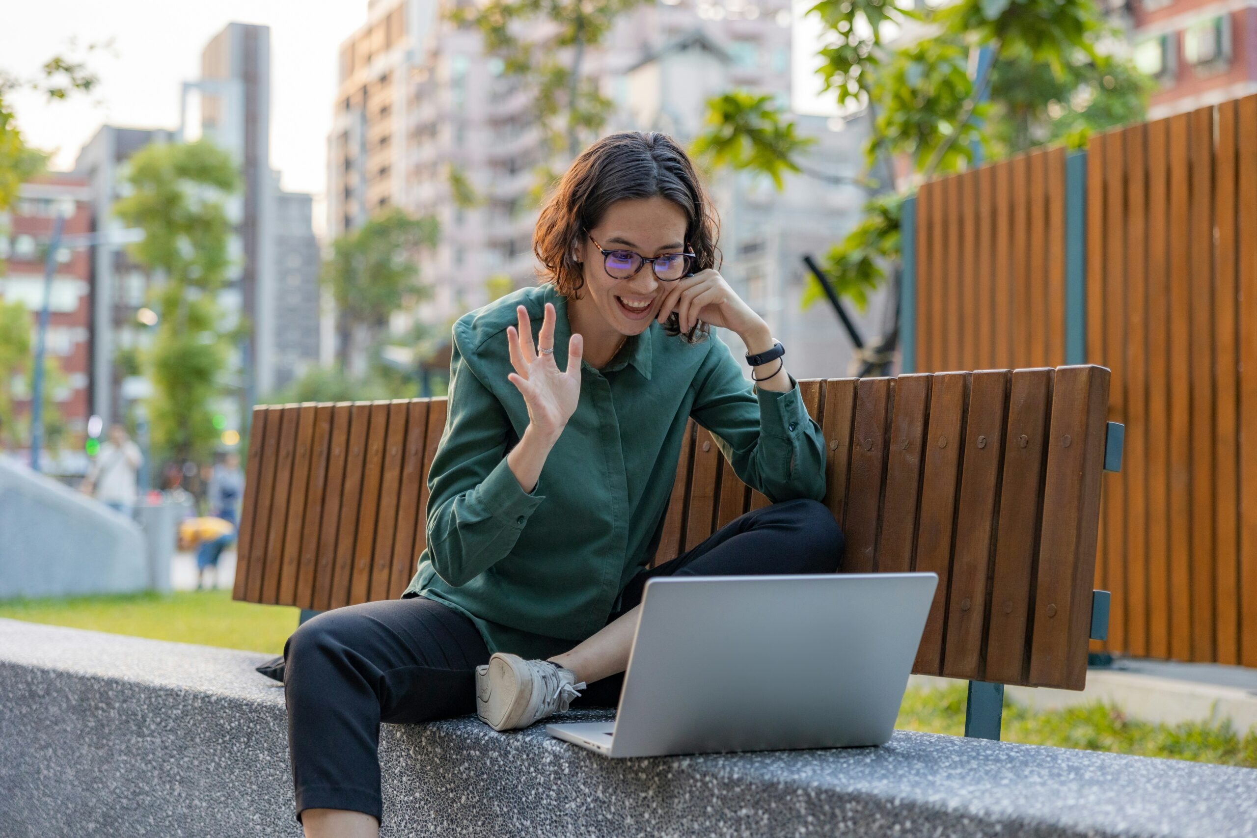 A young professional waving hello on a video call from her laptop, working outdoors.